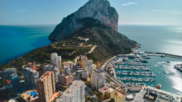 Вид з повітря на Кальпе, розташований на узбережжі Коста-Бланка в Іспанії, демонструє приголомшливий прибережний ландшафт, на якому домінує культова Пен-де-Іфач, масивне вапнякове скельне утворення, що височіє над Середземним морем. Коста-Бланка, провінція Аліканте, Іспанія.