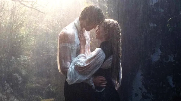 Джейкоб Елорді в ролі Гіткліффа та Марго Роббі в ролі Кеті у фільмі «Грозовий перевал» стоять у лісі та міцно обіймаються, поки на них падає дощ.