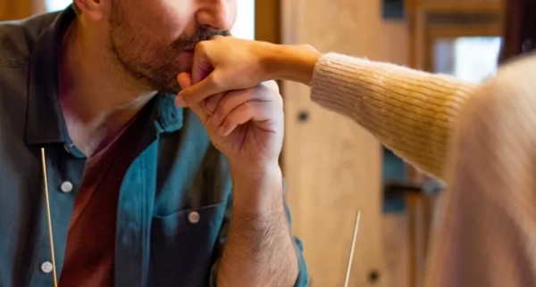 Закохана пара сидить у ресторані, подають їжу, а хлопець цілує руку своїй дівчині.