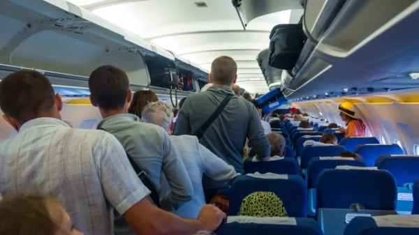 Люди стоять у проході, чекаючи на вихід з літака до відчинення дверей, поки інші пасажири залишаються на своїх місцях.