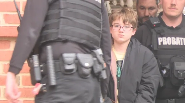 11-річного хлопчика в окулярах супроводжують інспектори пробації, коли його супроводжують до суду