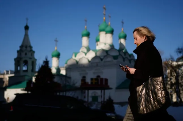 Жінка перевіряє свій телефон, йдучи вулицею в Москві