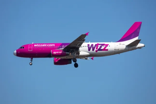 Літак Wizz Air з рожево-фіолетовим брендуванням летить у блакитному небі.