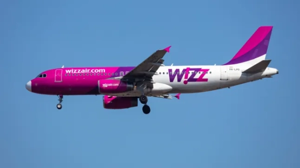 Літак Wizz Air з рожево-фіолетовим брендуванням летить у блакитному небі.